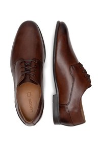 Brūni ādas kleitas apavi ar gludu apdari, auklu dizainu un šauru profilu. Iezīmē melnu gumijas zoli un toņu šuvumu.