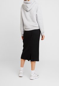 Sweat à capuche gris avec ourlet côtelé, associé à une jupe midi noire côtelée avec une fente latérale. Porté avec des baskets blanches et des chaussettes.