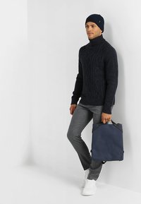 Suéter de punto navale, pantalones grises, zapatillas blancas y un bolso azul oscuro con detalles negros. Texturas suaves, diseño ajustado.