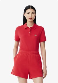 Röd polo skjorta med korta ärmar, med krage och Lacoste-logotyp, i kombination med matchande röda shorts med elastisk midja.