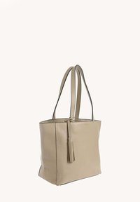 Sac en cuir beige de forme tote avec deux poignées, un pendentif décoratif et un design minimaliste. Il possède une texture lisse et une forme structurée.