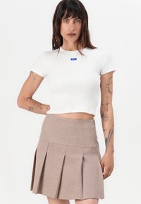 White cropped t-shirt with a blue logo, paired with a brown pleated skirt. Smooth texture and fitted design. Minimalist style and detailing.