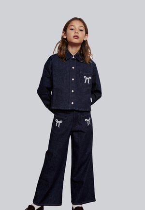 Conjunto de chaqueta y pantalones de mezclilla azul marino con bordado de lazo blanco en los bolsillos; diseño con cuello y cierre de botones; ajuste holgado y textura suave.