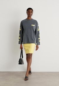 Gray long-sleeve sweatshirt with yellow heart prints on sleeves, paired with a yellow pencil skirt. Model carries a black handbag and wears black sandals.