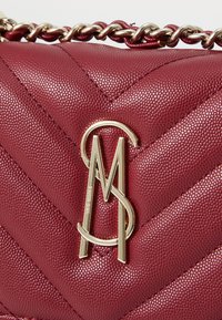 Crimson handbag made from textured leather with a chevron pattern. Features a gold-tone logo and chain strap for carrying.