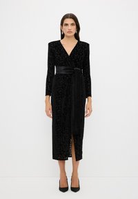 Schwarzes Wickelkleid aus strukturiertem Stoff mit floralem Muster, langen Ärmeln, einem V-Ausschnitt und einem gebundenen Gürtel in der Taille. Knielange Schnittform.