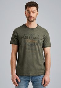 T-shirt en coton vert olive avec col rond, présentant un logo imprimé 'PME LEGEND Catalina' en marron foncé et accents orange clair.