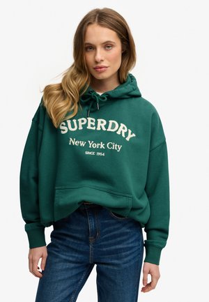 Zielona bluza z kapturem ze sznurkiem, z dużym białym logo "SUPERDRY" oraz napisem "New York City". Przód z kieszenią kangurką, luźny krój.