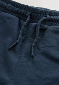 Tengerészkék pamut melegítőnadrág elasztikus derékpánttal és húzózsinórral. Sima textúrájú, kényelmes szabású, minimális varrási részletekkel.