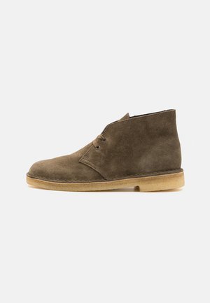 Bottines en daim marron avec un bout arrondi, deux œillets pour les lacets, une tige texturée et une semelle en caoutchouc de couleur claire.