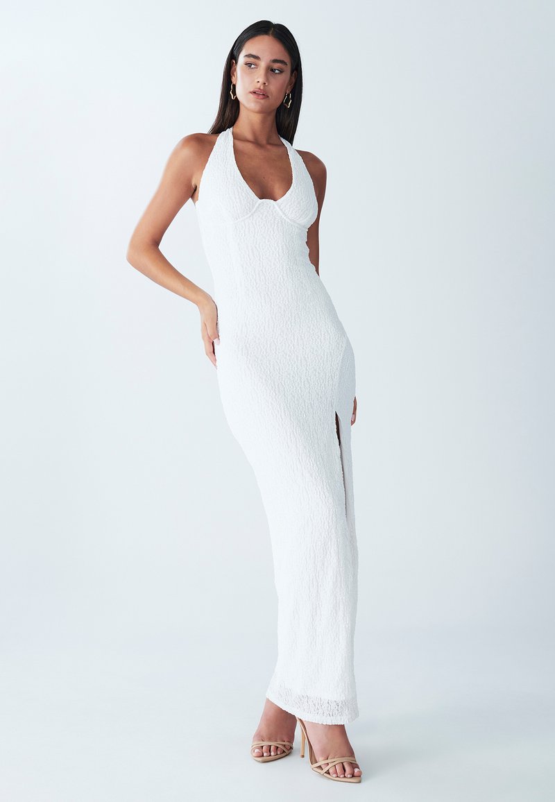 Kostum putih dengan leher halter, terbuat dari kain tekstur, potongan ramping, belahan di samping, dan siluet panjang. Dipadukan dengan heels telanjang dengan tali.