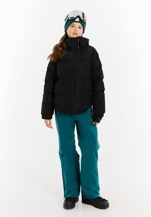 Schwarze, gepolsterte Jacke mit Reißverschluss, kombiniert mit türkisfarbenen Schneehosen. Eine türkisfarbene Mütze und ein verspiegeltes Goggles vervollständigen das Winter-Sportoutfit.