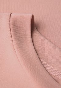Světle růžová žebrovaná tkanina s hladkým povrchem, která ukazuje skládací límec a švy, zdůrazňující minimalistický design.