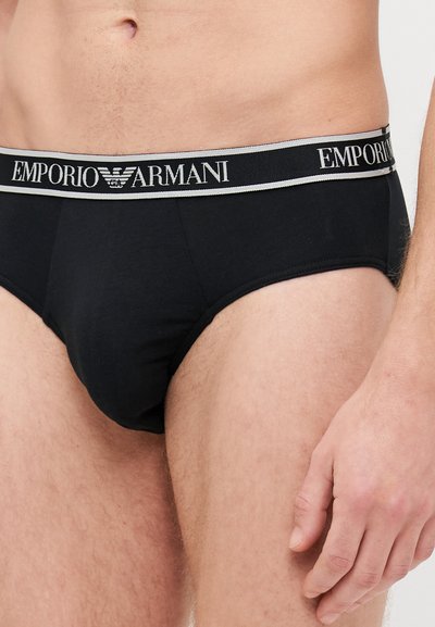 Slip in cotone nero con fascia in contrasto grigia che presenta il logo "Emporio Armani". Texture liscia e vestibilità aderente, tipica del design dell'abbigliamento intimo maschile.