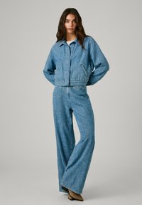 Light blue denim jacket with a cropped design and front pockets, paired with matching wide-leg trousers. Smooth texture, classic styling.