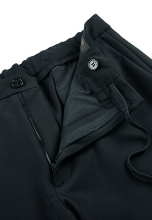 Pantalons noirs avec fermeture éclair ouverte, bouton et taille à cordon sur fond blanc.