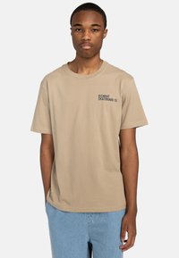 Beige Baumwoll-T-Shirt mit kurzen Ärmeln, Rundhalsausschnitt und kleinem gesticktem "Element Skateboard Co."-Logo auf der linken Brust.