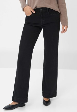 Schwarze Denim-Hosen mit geradem Bein, mittelhoher Taille, zwei frontalen Taschen und dezenten Nähdetails. Getragen mit schwarzen Ballerinas.