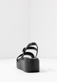 Sandalo nero con piattaforma, cinturino regolabile, texture liscia, apertura sul retro e tacco largo per stabilità. Design minimalista.
