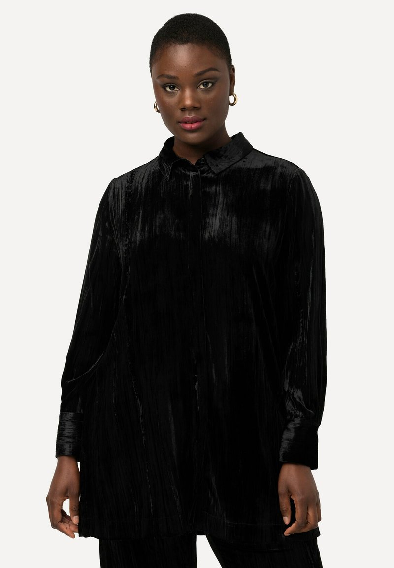 Camicia in velluto nero con colletto, maniche lunghe e vestibilità ampia. Presenta una trama verticale e chiusura con bottoni.