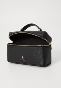 Trousse de maquillage en cuir noir avec une finition texturée, zipper doré et poignée supérieure. L'intérieur est doublé de tissu noir. Présente un logo doré.