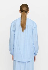 Camicia a righe blu chiaro con maniche lunghe, schiena plissettata e polsini elastici. Realizzata in tessuto di cotone, presenta una vestibilità comoda e un orlo arrotondato.