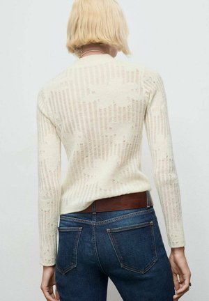 Suéter de punto en crema claro con rayas verticales y textura calada. Mangas largas y cuello redondo. Combinado con jeans azul oscuro.