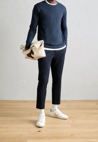 Granatowa koszula z długim rękawem z białym kołnierzykiem, czarne spodnie, białe sneakerzy oraz beżowa torba na ramię z złożonym wzornictwem.