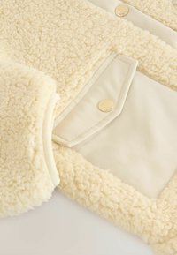 Kermakunden pelti, jossa on sileä sisävuori, kultaisilla niittikannoilla ja laskostetulla taskulla.