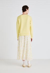 Gul genser med lange ermer, kombinert med en plissert blomstrete maxiskjørt i hvitt og gult. Myk tekstur, avslappet passform, og enkelt design.