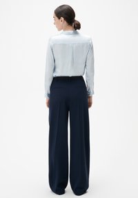 Blouse en satin bleu clair à manches longues avec un col subtil, associée à un pantalon large taille haute en navy avec une texture lisse et des poches arrière.