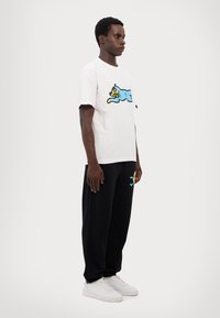 Hvid bomulds t-shirt med et blåt tegneseriekatte grafik, sammen med sorte joggingbukser med en farverig tegneseriefigur broderi. Hvide sneakers.