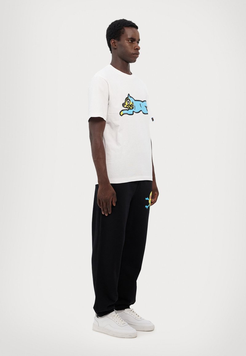 Hvid bomulds t-shirt med et blåt tegneseriekatte grafik, sammen med sorte joggingbukser med en farverig tegneseriefigur broderi. Hvide sneakers.