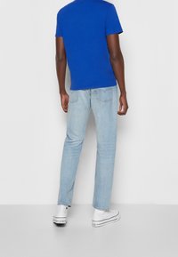Blue short-sleeve t-shirt, light blue jeans, and white sneakers. The t-shirt is plain, the jeans have a straight cut with back pockets.