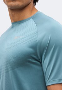 Mann trägt hellblaues Sportshirt mit subtiler Strukturierung und kleinem Nike-Swoosh auf der Brust.