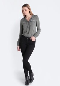 Oliwkowa, długosleeve'owa koszula z zapinanym przodem i dwoma kieszeniami na piersi, w połączeniu z czarnymi skinny jeansami i botkami za kostkę. Gładka faktura materiału.