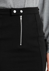 Svart pennkjol med dragkedja fram, två tryckknappar i midjan och en lätt elastisk tygstruktur.