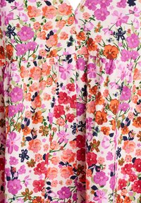 Gros plan sur un tissu à motif floral dense avec des fleurs roses, orange, rouges, violettes et des tiges vertes sur fond blanc.