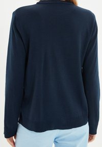 Marineblauer Strickpullover mit einem gerippten Kragen, langen Ärmeln und einer lockeren Passform. Glatte Textur mit einem Saum, der an den Seiten sanft abgerundet ist.