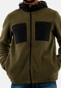 Fleecejacke in Olivgrün mit schwarzen Nylon-Reißverschlusstaschen auf der Brust und einer Kapuze. Verfügt über einen durchgehenden Frontreißverschluss und taillierte Bündchen.