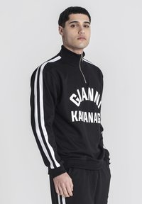 Čierny zipsový mikina s bielym nápisom "GIANNI KAVANAGH." Špeciálne biele pruhy na rukávoch a vysoký golier. Hladká textúra, voľný strih.
