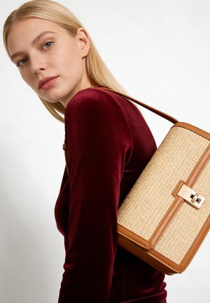 Blonde vrouw met een aansluitende bordeauxrode fluwelen top, en een beige en bruine gevlochten schoudertas met gouden sluiting.