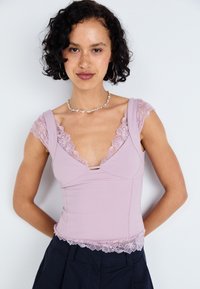 Lilac tank top dengan aksen renda di bahu dan hem. Memiliki leher V yang dalam dan desain yang pas. Tekstur halus dan kain yang lembut.