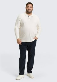 Weißes Langarm-Polohemd mit Kragen, kombiniert mit dunkelblauen Hosen und weißen Sneakers. Lässiger Schnitt mit strukturiertem Stoff.