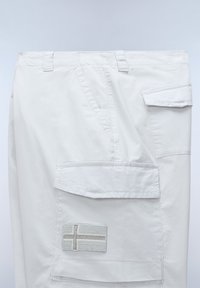 Pantalon cargo blanc avec plusieurs poches, dont une grande poche à rabat ornée d'un patch cousu en forme de croix nordique.