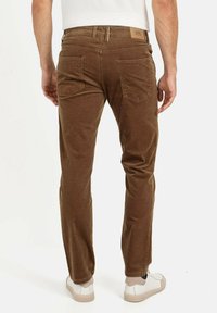 Pantalons en velours côtelé marron avec une coupe slim, dotés de poches au dos et d'une étiquette en cuir griffée au niveau de la taille. Portés avec des baskets blanches.