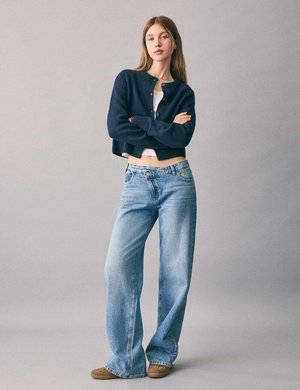 Cárdigan corto navy, camiseta blanca, pantalones de pierna ancha azul claro y zapatos de gamuza color beige; tejido suave con cierre de botones y bordes deshilachados.