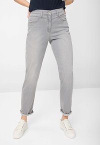Lys grå jeans med lige ben-design, der har forlommer, optrukne cuffs og en enkelt knaplukning. Båret sammen med hvide sneakers.