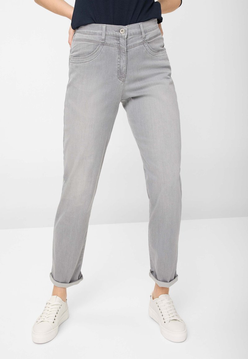 Lys grå jeans med lige ben-design, der har forlommer, optrukne cuffs og en enkelt knaplukning. Båret sammen med hvide sneakers.