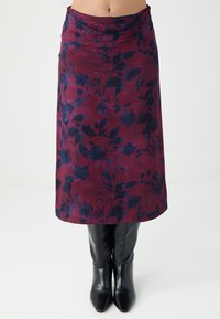 Bordeauxfarbener Rock mit dunkelblauem Blumenmuster, glatter Textur, knielang, mit einem gerafften Bund. Schwarze Stiefel mit Absatz darunter.